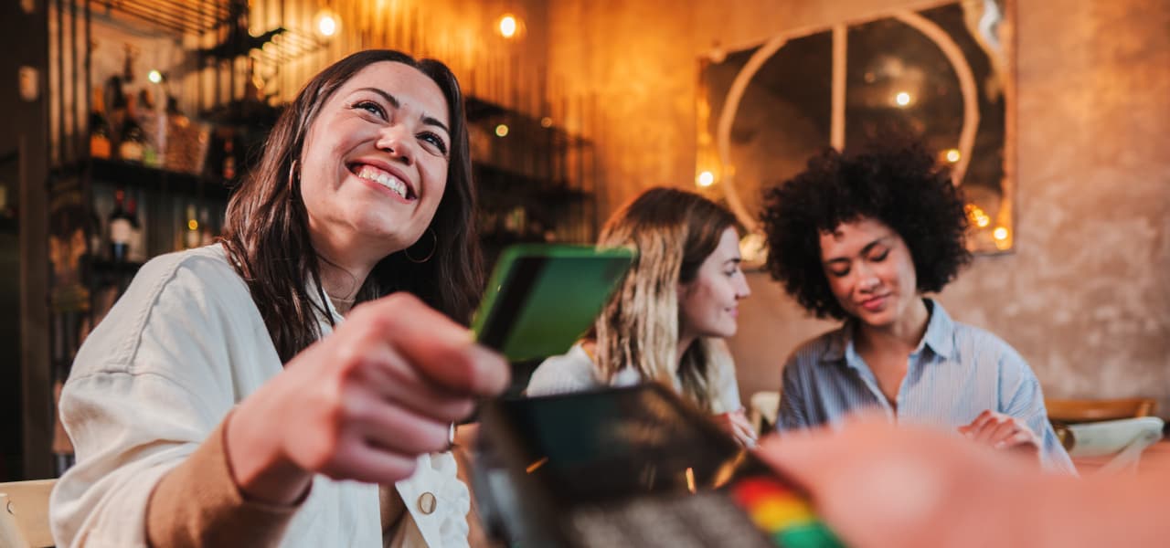 A Restaurant 1 Header (jpg) | Motiv ©Jose Calsina-stock.adobe.com | © stock.adobe.com, Juli 2019 Eine junge Frau bezahlt in einem Restaurant kontaktlos mit Kreditkarte. Sie lächelt und hält ihre Kreditkarte in der Hand. | Motiv ©Jose Calsina-stock.adobe.com | © stock.adobe.com, Juli 2019